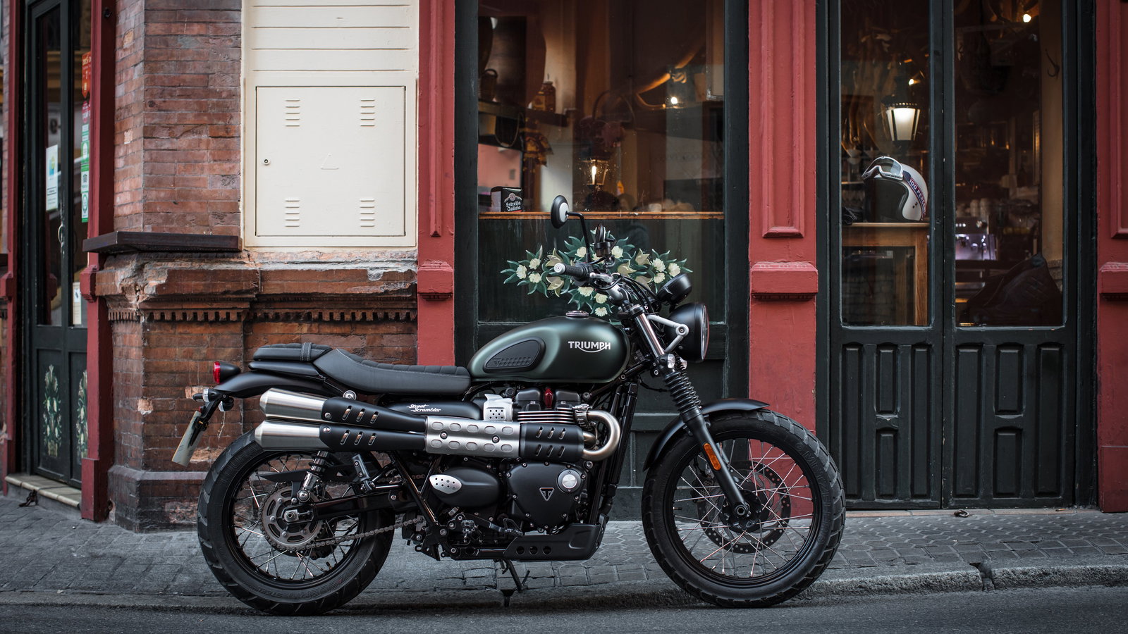 A Triumph Street Scrambler parked on a street outside a cafe